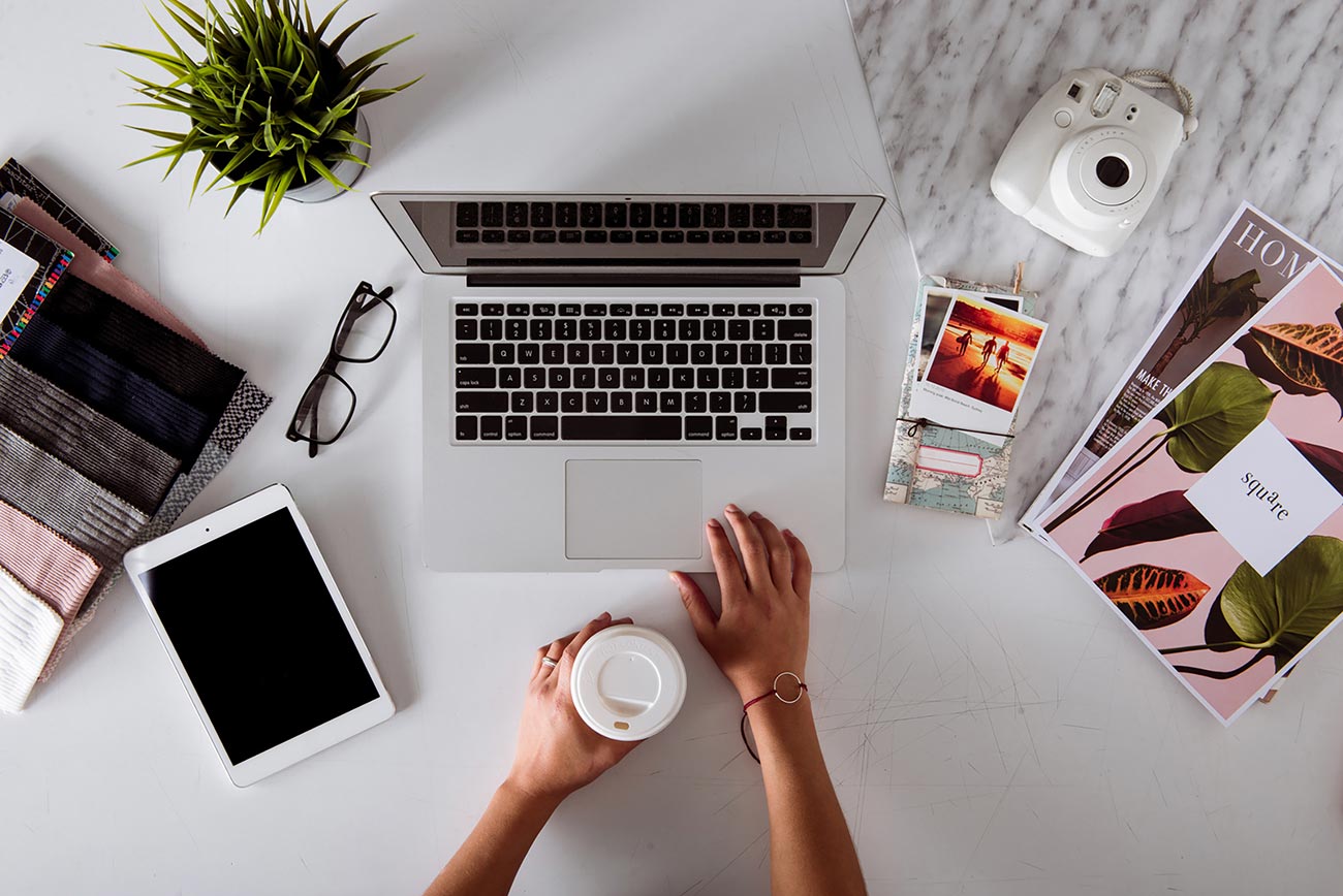 Flat lay of a clean and chic work desk: Ipad, Laptop, Camera, Magazines and Eyeglasses