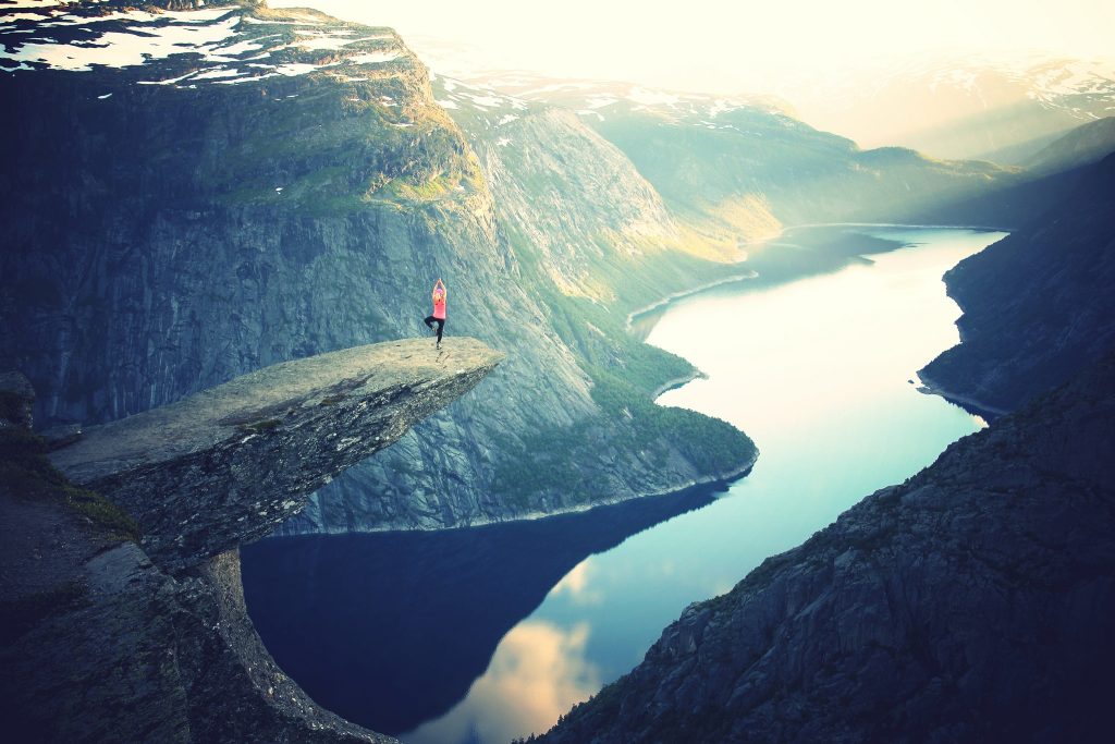 Woman doing yoga exercises on top of mountain edge