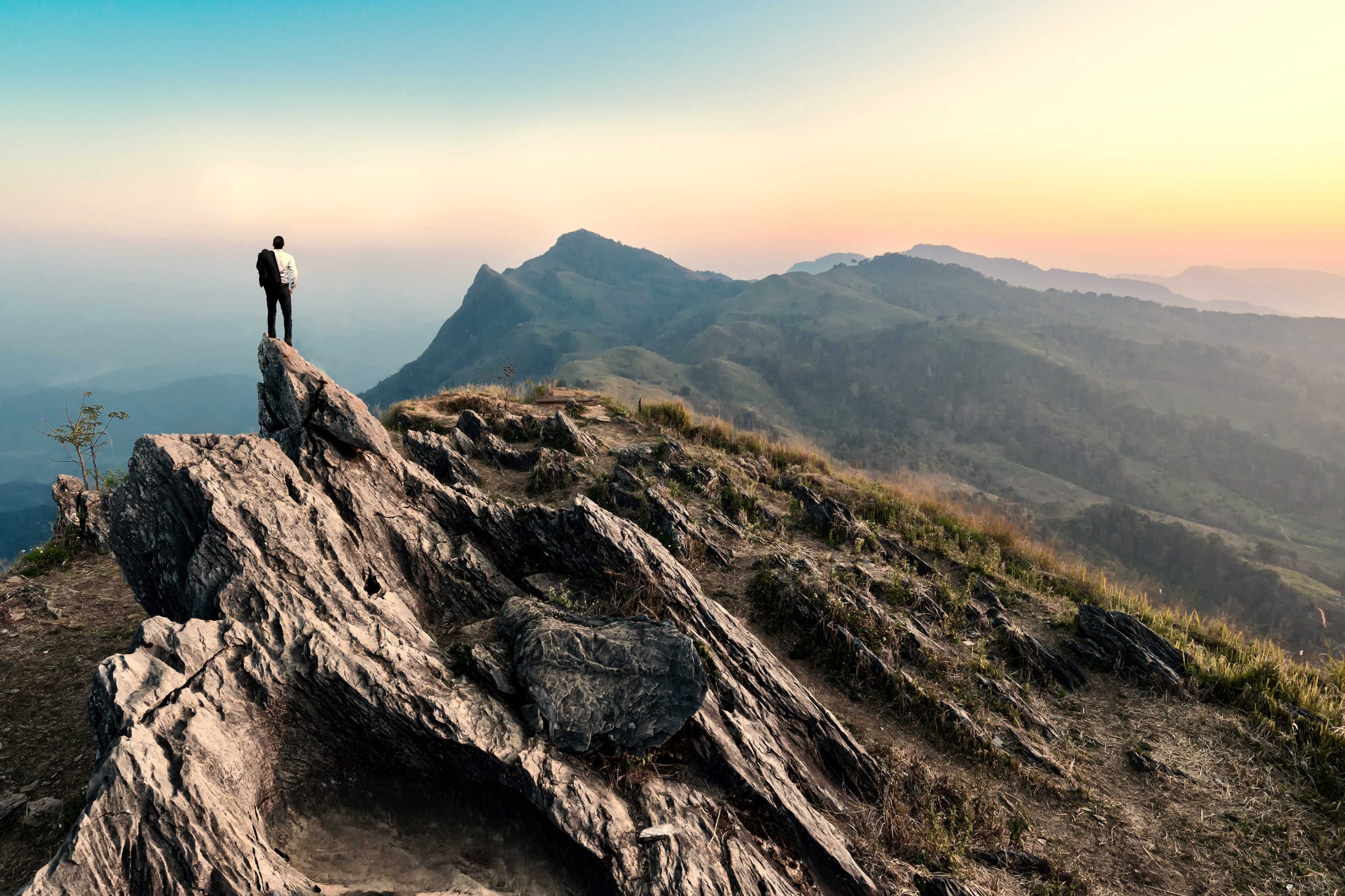 Businessman hike on the peak of rocks mountain at sunset
