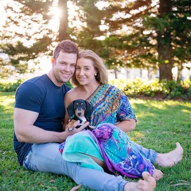 Brittany and Cory with their sausage dog Armani sitting on the grass