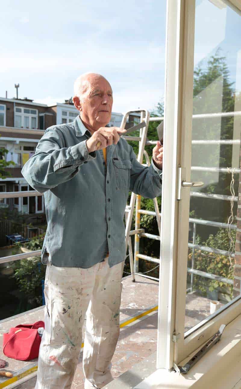 Elderly man paints a house